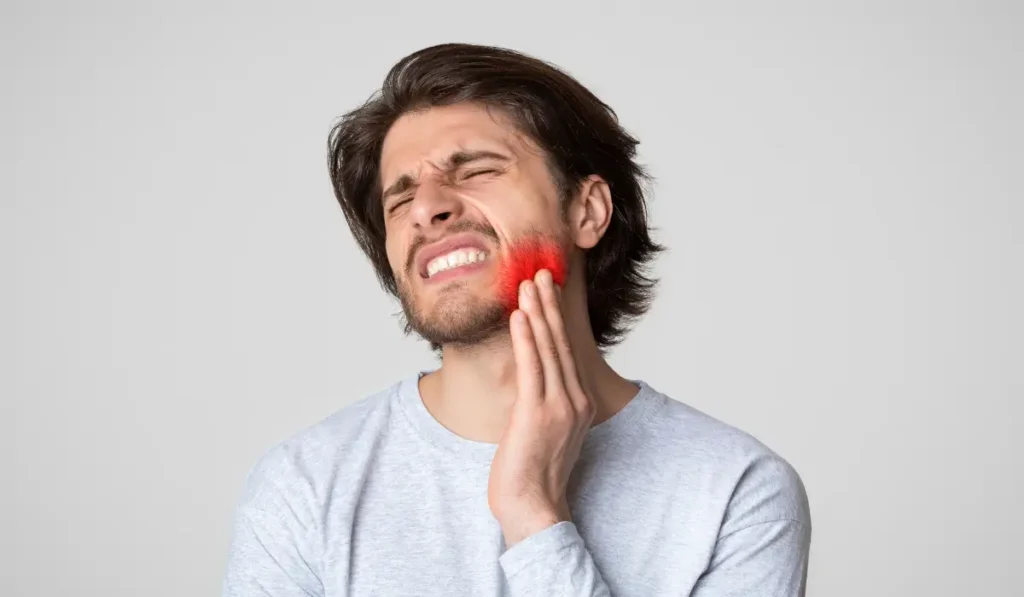 Young man holding face showing jaw pain caused by nighttime bruxism and ongoing teeth clenching during sleep.