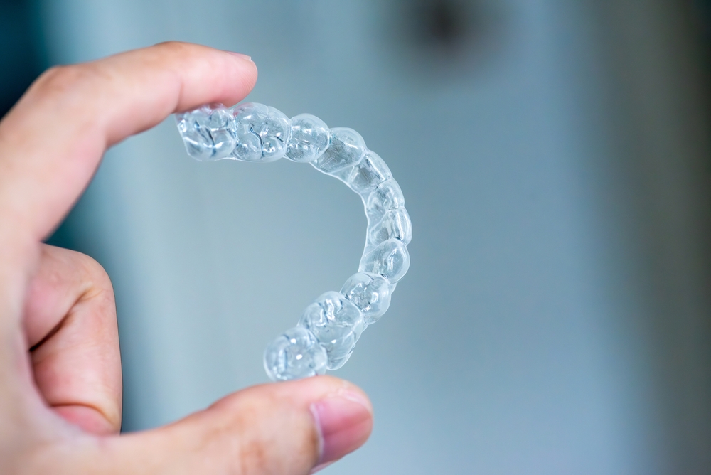 Close-up of a hand holding a clear plastic dental aligner tray for teeth straightening.