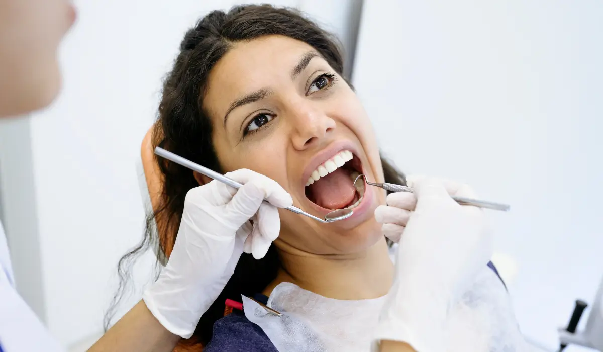Dental Hygienist examining an adult patient's teeth and gums with a dental mirror and explorer during a routine preventive dental examination. Show less